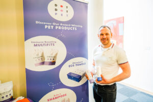DotDotPet Founder Harry Chapman at the Business of Pets Conference 2024 holding his product innovation in front of a branded promotional banner.