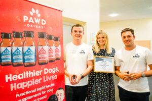 PAWD Drinks founders Rory & Archie at the 2024 Business of Pets Conference holding their product innovation in front of a branded promotional banner.